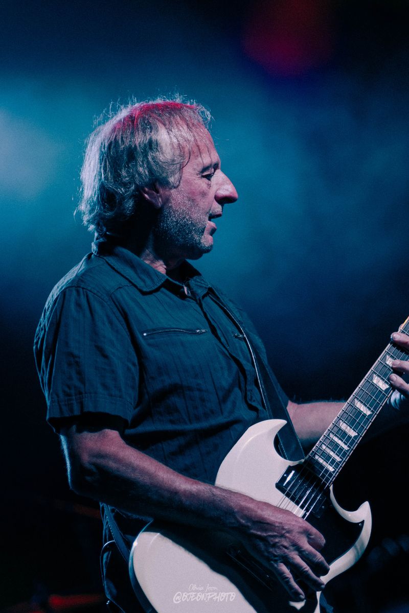 Guitarist in profile playing a white SG in teal light