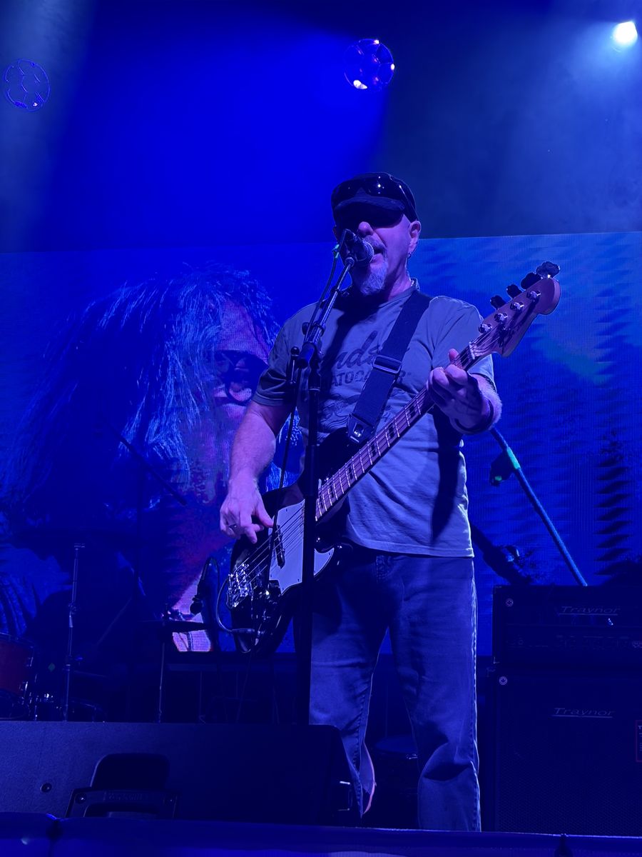 Bassist singing at the mic in front of a blue video screen