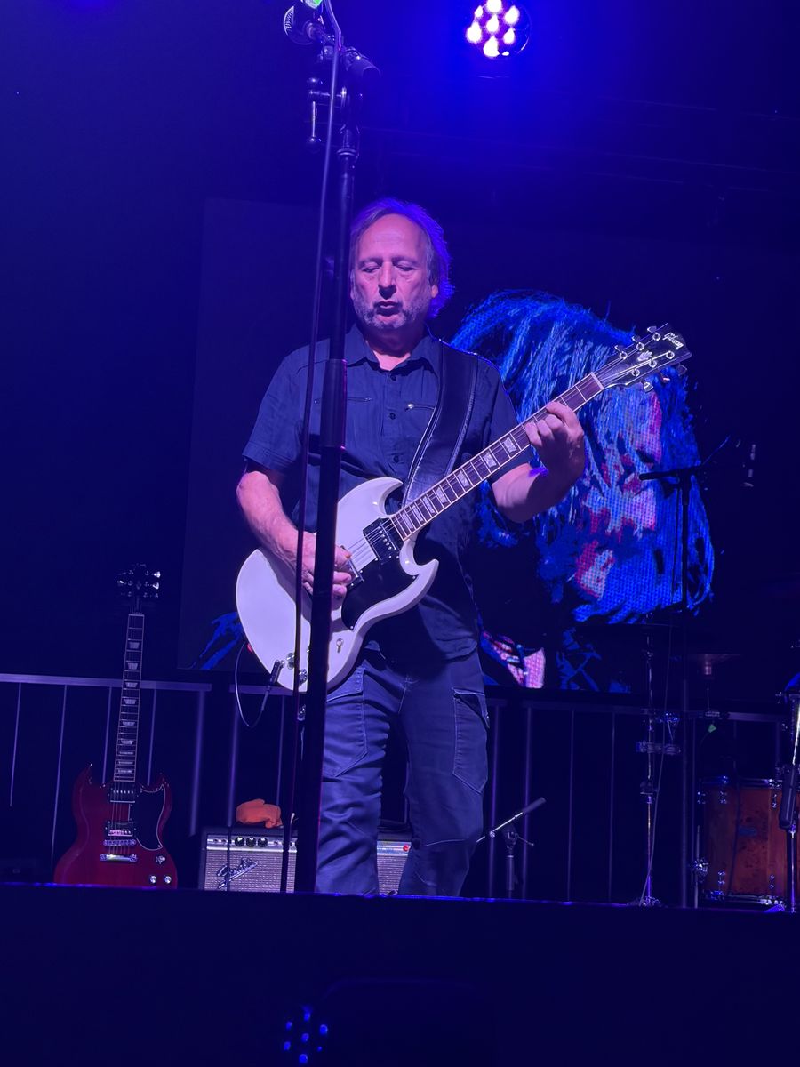 Guitarist with a white SG behind a mic stand in purple light